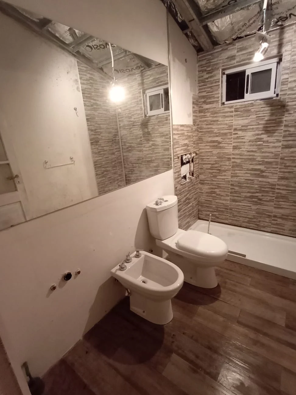 Baño terminado por LM Construction, con revestimiento de piedra, sanitarios y mampara de ducha
